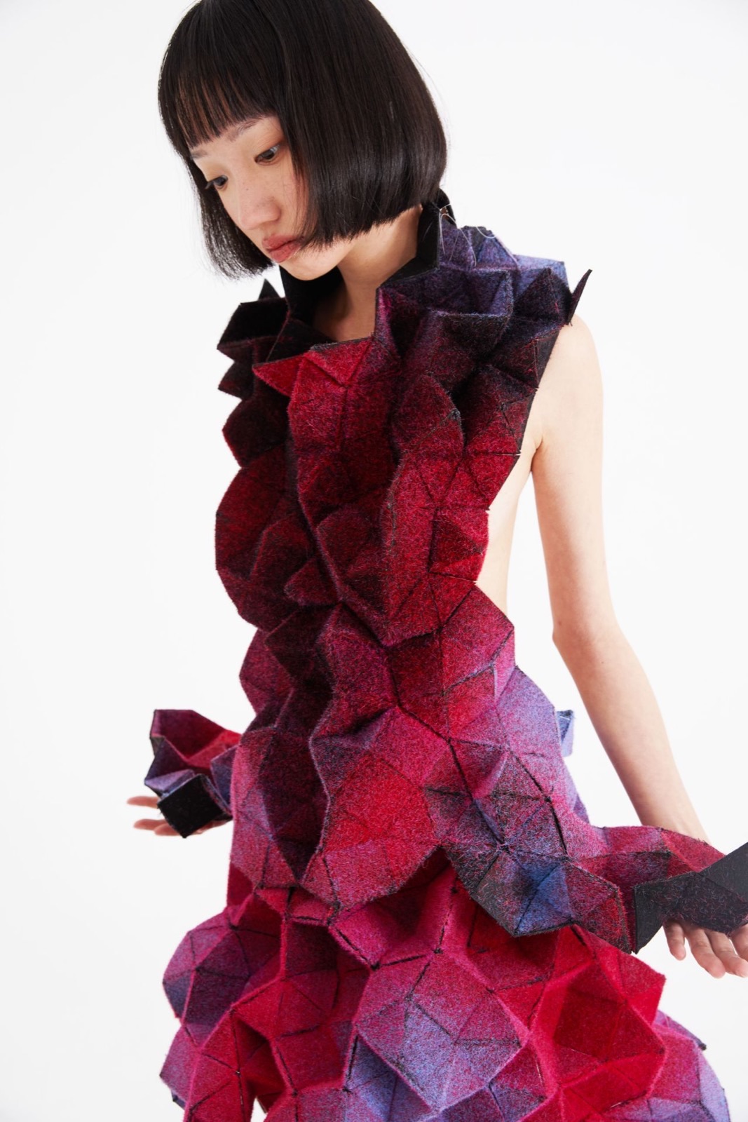 A wool felt garment of hand-stitched squares and triangles in a red-to-violet gradient